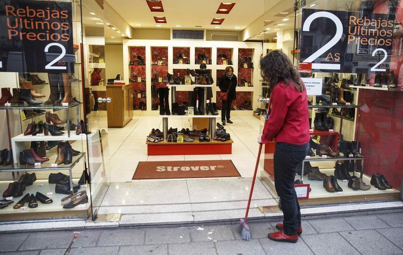 Women look at shoes inside a store as a worker sweeps the street outside, in Madrid January 29, 2015. Spanish retail sales leapt 6.5 percent year-on-year on a calendar-adjusted basis in December, the biggest increase since 2003 as Spaniards spent more freely encouraged by an improving economic outlook and falling oil prices. REUTERS/Andrea Comas (SPAIN - Tags: BUSINESS TEXTILE)