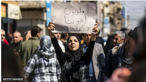 Una mujer sostiene un cartel que dice en árabe "Los alauitas son nuestros hermanos y familia" durante una manifestación multitudinaria en la ciudad de Qamishli, en el noreste de Siria.