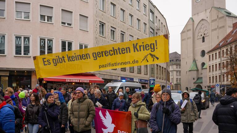 Manifestación en Múnich contra el servicio militar obligatorio en Alemania. Una multitud de manifestantes sostiene una gran pancarta amarilla con texto en alemán negro que dice "No hay guerra justa" - rnd